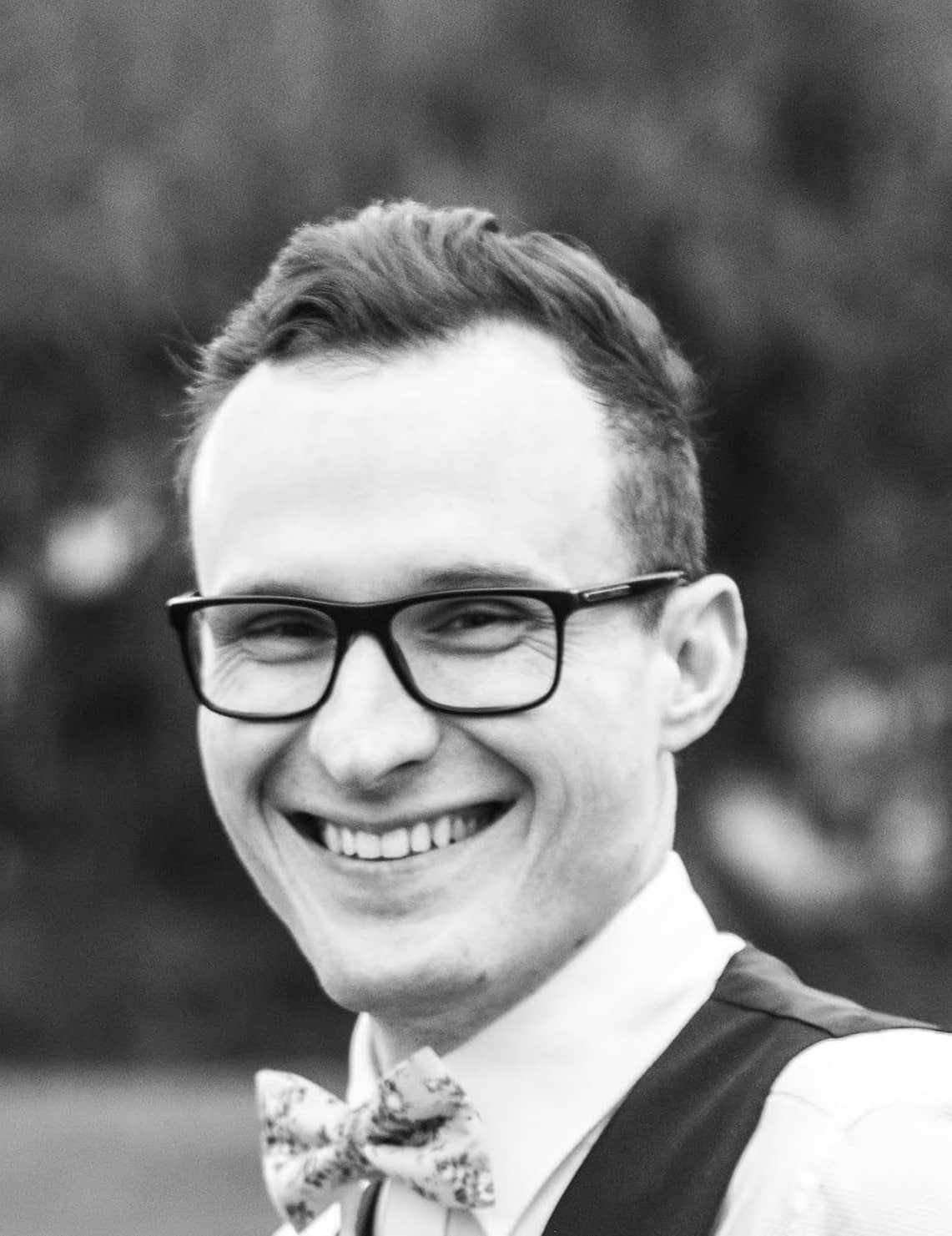 A smiling man wearing glasses and a bow tie, exuding a friendly and approachable demeanor.