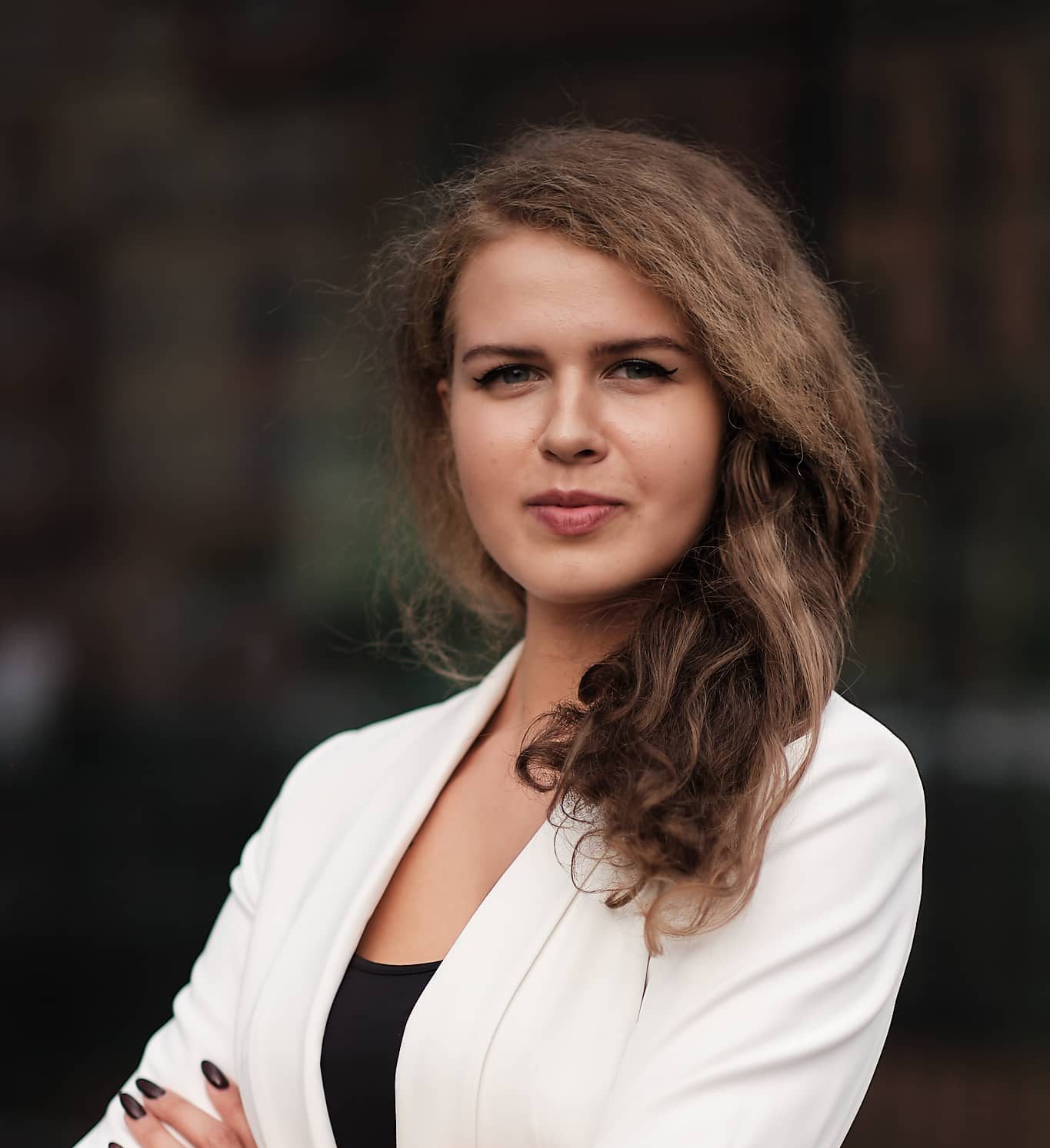 A woman wearing a white blazer over a black top, standing confidently with a neutral expression.