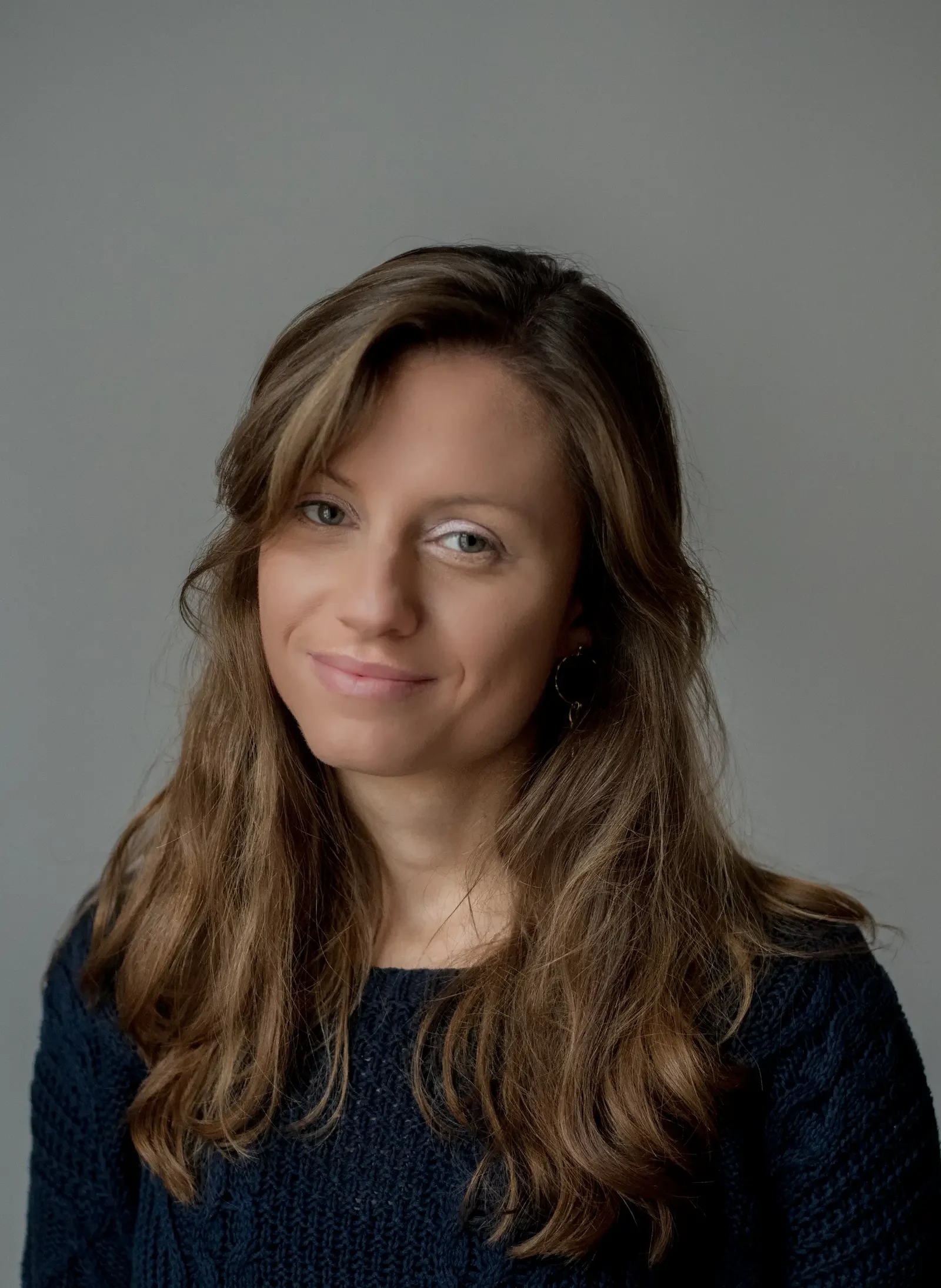 A woman with long hair wearing a cozy sweater, smiling softly at the camera.